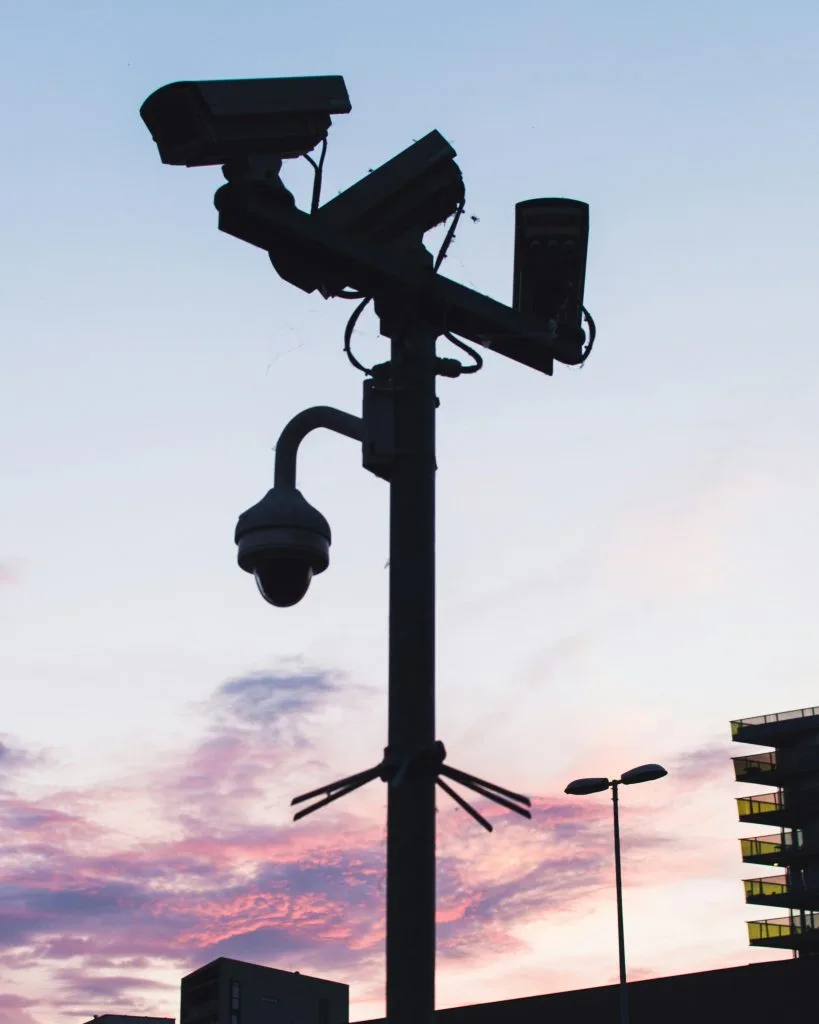 Permanent outdoor lighting enhances security with a silhouetted camera against a vibrant sunset sky